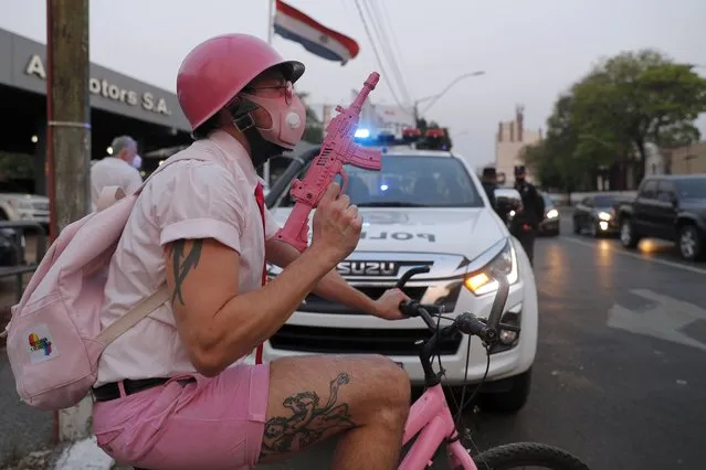 Holding a toy machine gun and wearing a mask to curb the spread of the new coronavirus, a gay man perfoms for peace in front of a police car during a LGTBI Pride caravan in Asuncion, Paraguay, Wednesday, September 30, 2020. LGTBI organizations celebrated their Pride day with a caravan of vehicles because of the ongoing COVID-19 pandemic. (Photo by Jorge Saenz/AP Photo)