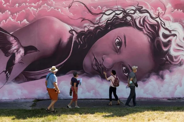 Tourists look at a graffiti as they visit the Street Art City in Lurcy-Levis, centre France, on September 3, 2020. (Photo by Thierry Zoccolan/AFP Photo)