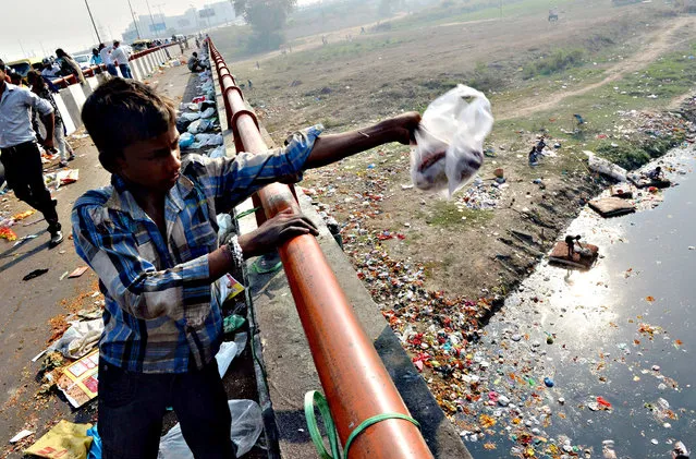 An Indian boy throws domestic garbage into the already polluted Yamuna river in New Delhi on October 23, 2015. Considered one of the holiest rivers in India, the Yamuna River has been dying a slow death from pollution for decades despite the investment of millions of dollars to preserve its ecosystem. (Photo by Prakash Singh/AFP Photo)