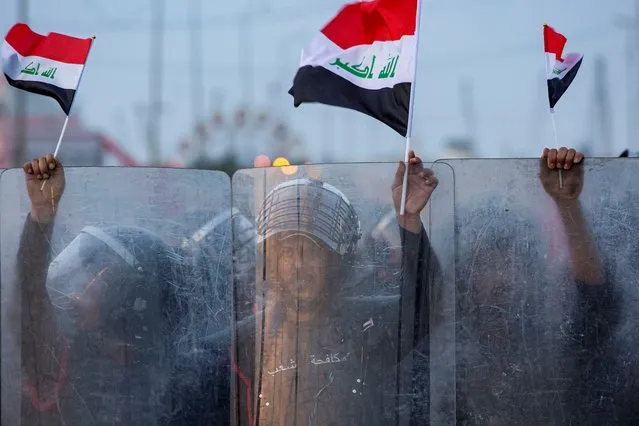 Iraqi riot policemen wave national flags as they form a barrier while anti-government demonstrators gather for a protest by the local administration building in the southern city of Basra on November 7, 2020, after a protester was killed the previous day. Omar Fadhel, a young demonstrator, was shot dead in the southern Iraqi city of Basra on November 6 as gunmen killed an activist in the capital, police and medics said. (Photo by Hussein Faleh/AFP Photo)