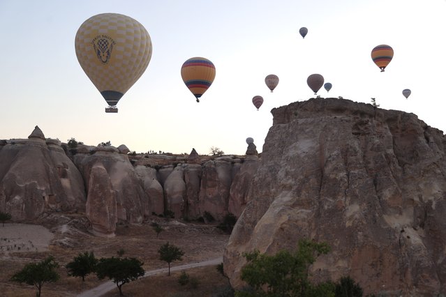 Hot air balloons take off at sunrise, creating stunning views over the valleys of Cappadocia, in Nevsehir, Turkiye on July 14, 2025. Listed as a UNESCO World Heritage Site, Cappadocia captivates visitors with its natural formations and cultural heritage, offering activities such as hiking, balloon tours, and rural excursions that attract numerous domestic and foreign tourists throughout the year. (Photo by Behcet Alkan/Anadolu via Getty Images)