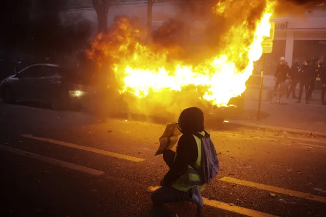 A protester kneels in front of a burning car during a demonstration, Saturday, December 5, 2020 in Paris. (Photo by Lewis Joly/AP Photo)