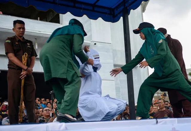 Sharia police officers prepare a woman to be publicly flogged in front of a mosque in the provincial capital Banda Aceh on April 20, 2018. A group of amorous couples and prostitutes were publicly whipped for breaking Islamic law in Indonesia' s Aceh province on April 20, just a week after it pledged to take the widely condemned practice indoors. (Photo by Chaideer Mahyuddin/AFP Photo)
