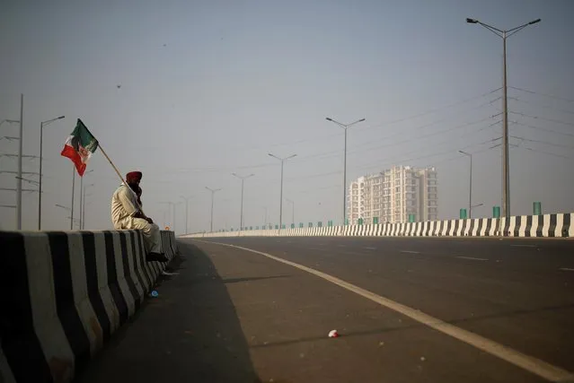 A farmer holds a flag as he sits on an empty blocked highway during a nationwide strike against the newly passed farm bills at the Delhi-Uttar Pradesh border in Ghaziabad, India, December 8, 2020. (Photo by Adnan Abidi/Reuters)