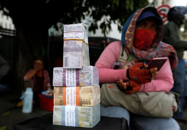 A woman who makes change for large bank notes sits beside stacks of Indonesian Rupiah notes in a street in Jakarta, Indonesia April 27, 2018. (Photo by Willy Kurniawan/Reuters)