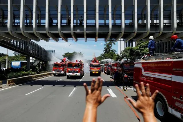 A firefighter gestures to fellow firefighters to stop spraying disinfectant in order to refill their tanks, as the disinfectant is integral in the prevention of the spread of the coronavirus disease (COVID-19), on the main road in Jakarta, Indonesia, March 31, 2020. (Photo by Willy Kurniawan/Reuters)
