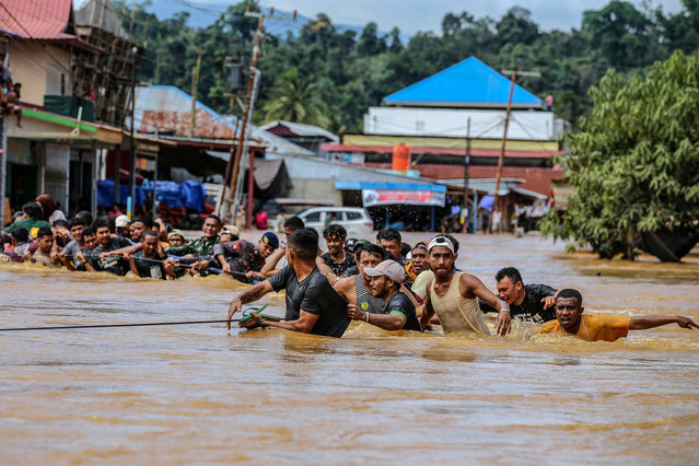 People holding a rope wade across flood water after the Kobe River overflowed following heavy rains in Lukulamo, North Maluku, Indonesia on July 22, 2024. (Photo by Azzam Risqullah/AFP Photo)