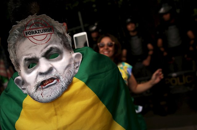 A demonstrator wears a mask depicting Brazil's former president Luiz Inacio Lula da Silva as he takes a picture of a woman in front of riot police during a protest calling for the impeachment of Brazil's President Dilma Rousseff in Sao Paulo, Brazil, December 13, 2015. (Photo by Nacho Doce/Reuters)