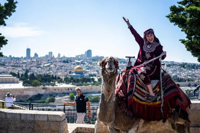 A tourist poses for photos riding a camel on the Mount of Olives overlooking the old city of Jerusalem on June 12, 2023. (Photo by Jewel Samad/AFP Photo)