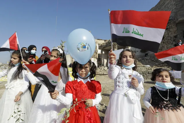 Children in their festive garment wave Iraqi flags to the camera as they arrive to join Pope Francis who will pray for the victims of war at Hosh al-Bieaa Church Square, in Mosul, Iraq, once the de-facto capital of IS, Sunday, March 7, 2021. (Photo by Andrew Medichini/AP Photo)