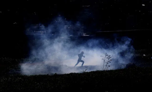 A Palestinian demonstrator runs to seek cover from tear gas fired by Israeli soldiers, during a demonstration against Israel's settlements in the village of Bet Dajan near the northern West Bank city of Nablus, 12 February 2021. (Photo by Alaa Badarneh/EPA/EFE)