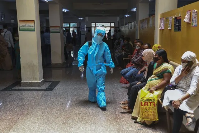 An Indian woman in personal protective suit walks towards a COVID-19 ward of a hospital as others waits for their test results in Hyderabad, India, Thursday, April 29, 2021. (Photo by Mahesh Kumar A./AP Photo)