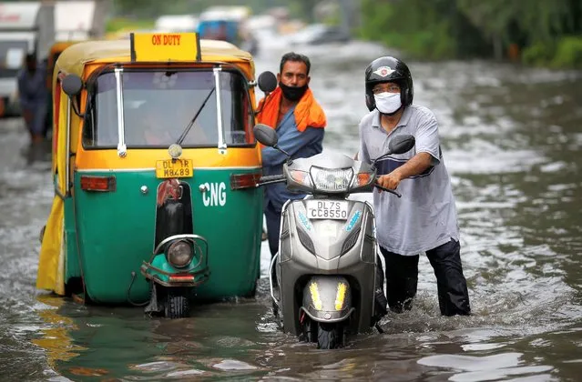 Commuters pull their vehicles through a waterlogged road after heavy rains in New Delhi, India, July 27, 2021. (Photo by Adnan Abidi/Reuters)