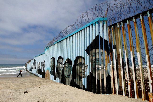 An interactive mural portraying the faces of deported migrants, who arrived to the United States as children, covers a section of the border fence as part of the “Playas de Tijuana Mural Project” in which spectators can read their migration stories by using a QR code placed next to the different portraits, in Tijuana, Mexico, August 4, 2021. (Photo by Jorge Duenes/Reuters)