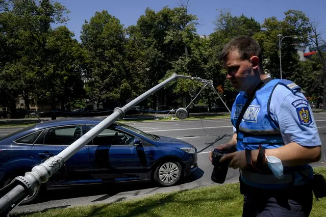A Romanian gendarme takes pictures of a damaged car after a lamppost was knocked down by a U.S military Black Hawk helicopter following an emergency landing on a busy boulevard, in Bucharest, Romania, Thursday, July 15, 2021. A U.S military Black Hawk helicopter that took part in preparations for Romanian Aviation day, which is set to take place on July 20, was forced to land on a busy Bucharest boulevard, Thursday morning, damaging two cars after knocking down two lampposts, no casualties were reported. (Photo by Andreea Alexandru/AP Photo)