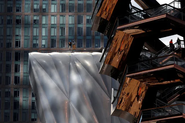 Workers are seen on “The Vessel” (R) comprised of 154  connected flights of stairs and 80 landings designed by Thomas Heatherwick and on “The Shed”  arts center (L) at the Hudson Yards development on Manhattan's West side, in New York City, New York, U.S., March 12, 2019. The Thomas Heatherwick design opens to the public Friday, March 15, 2019. (Photo by Mike Segar/Reuters)