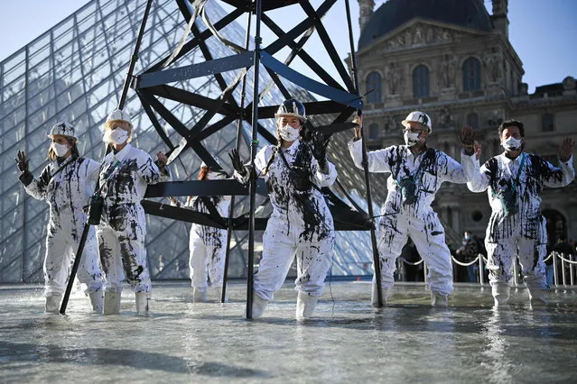 Greenpeace activists wearing the uniform of petroleum workers stand beside a smoking “oil well tower” during an action in front of The Louvre Museum Pyramid in Paris on October 6, 2021 as they protest against French energy company Total and continued world fossil fuel production and consumption. (Photo by Anne-Christine Poujoulat/AFP Photo)