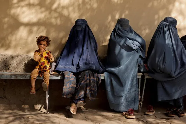 A girl sits with women wearing burqas outside a hospital in Kabul, Afghanistan on October 5, 2021. (Photo by Jorge Silva/Reuters)