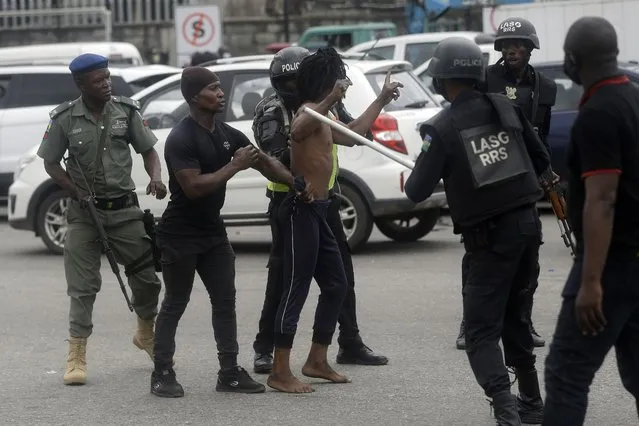 A protester is detained by police officers following a demonstration at Lekki Toll plaza in Lagos Nigeria Wednesday, October 20, 2021. Nigerian police officers fired tear gas at protesters in Lagos, the country's largest city, as they tried to disperse hundreds of people demonstrating against police brutality on Wednesday. One year ago, thousands marched in Nigeria for the #EndSARS movement to protest the activities of the now-disbanded Special Anti-Robbery Squad, a unit accused of police brutality. (Photo by Sunday Alamba/AP Photo)