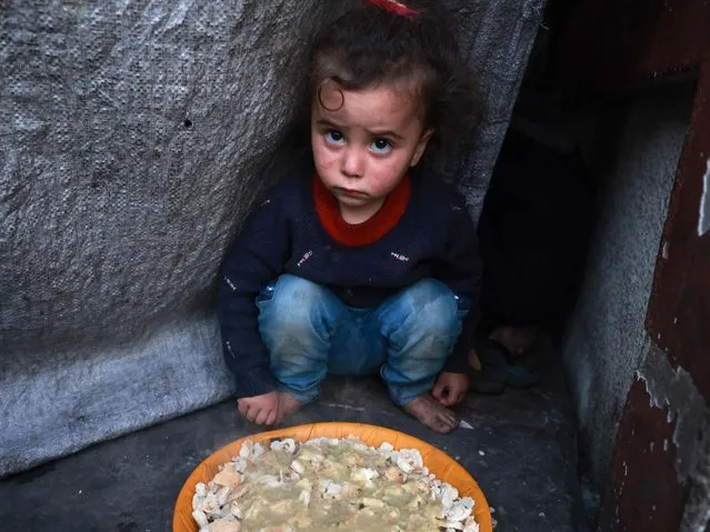 A Palestinian child sits next to a plate before an “iftar” meal, the breaking of fast, on the second day of the Muslim holy fasting month of Ramadan, at a shelter for displaced people in Rafah in the southern Gaza Strip on March 12, 2024, amid ongoing battles between Israel and the militant group Hamas. (Photo by Mohammed Abed/AFP Photo)