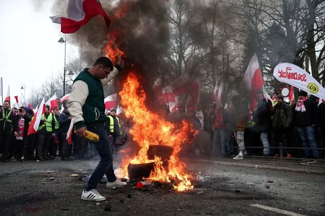 A man carries a Polish flag next to burning tyres, as farmers protest outside Polish Prime Minister Donald Tusk's office against the European Union's Green Deal and imports of Ukrainian agricultural products, in Warsaw, Poland on March 6, 2024. (Photo by Kacper Pempel/Reuters)