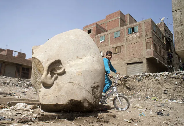 A boy rides his his bicycle past a recently discovered statue in a Cairo slum that may be of pharaoh Ramses II, in Cairo, Egypt, Friday, March 10, 2017. Archeologists in Egypt have discovered a massive statue that may be of pharaoh Ramses II, one of the country's most famous ancient rulers. The colossus, whose head was pulled from mud and groundwater by a bulldozer on Thursday, is around eight meters (yards) tall and was discovered by a German-Egyptian team. (Photo by Amr Nabil/AP Photo)