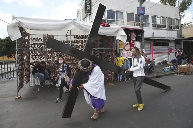 A Christian carries a cross in a reenactment of the crucifixion of Jesus Christ, in the Iztapalapa borough of Mexico City, Friday, April 2, 2021, amid the new coronavirus pandemic. Christians in Latin America mark Good Friday this year amid the coronavirus crisis with some religious sites open to limited numbers of faithful but none of the mass pilgrimages usually seen in the Holy Week leading up to Easter. (Photo by Marco Ugarte/AP Photo)