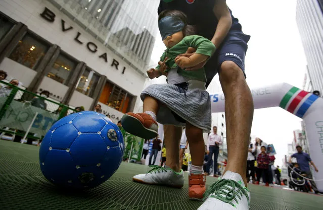 A young visitor experiences being blind as she kicks a ball during a blind football event in Tokyo's Ginza shopping district Monday, May 2, 2016. (Photo by Shizuo Kambayashi/AP Photo)