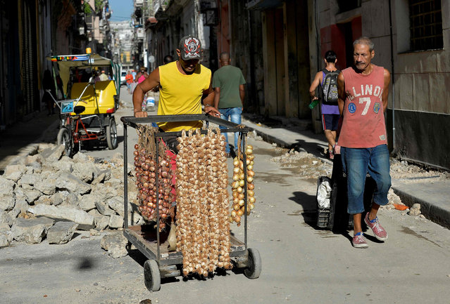 A man sells strings of garlic and onions in a street of Havana, on June 11, 2019. An official financial liquidity crisis since the end of 2018, has caused shortages of chicken, oil, flour and eggs, raising the spectre of a return to the “Special Period” – Cuba's hardest crisis in the 90s. The queues in the markets have decreased, as the government counteracts the shortage by making contingent purchases with resources from other budget items, but the prices – which have been rising recently- will not drop. (Photo by Yamil Lage/AFP Photo)