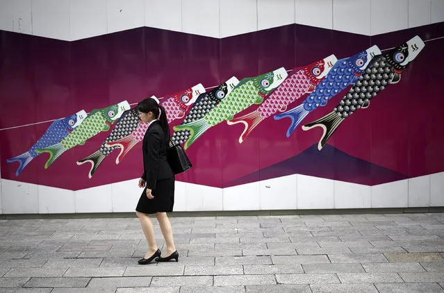 A woman walks near a wall painting featuring traditional carp streamers in Tokyo, Tuesday, May 3, 2016. The colorful streamers were hung to mark Children's Day on May 5, wishing children's healthy growth like carp that can swim up a waterfall. (Photo by Eugene Hoshiko/AP Photo)