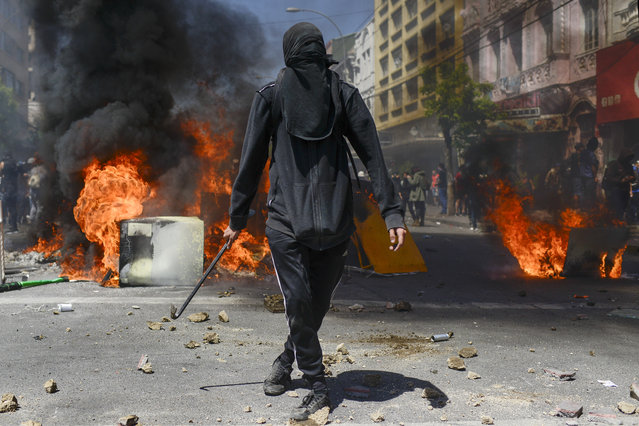 An anti-government protester stands in front of a burning barricade in Valparaiso, Chile, Thursday, October 24, 2019. President Sebastian Pinera made more economic concessions Thursday announcing a freeze on a 9.2% rise in electricity prices until the end of next year, to try to curb a week of deadly protests over price increases and other grievances. (Photo by Matias Delacroix/AP Photo)