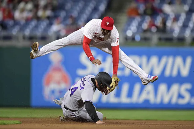 Philadelphia Phillies' Johan Camargo, top, leaps to avoid Colorado Rockies' Ryan McMahon, bottom, after turning a double play on a ball hit by Rockies' Brendan Rodgers during the seventh inning of a baseball game, Monday, April 25, 2022, in Philadelphia. (Photo by Derik Hamilton/AP Photo)