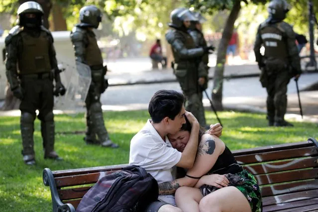 A man comforts a woman next to members of security forces during a protest against Chile's government in Santiago, Chile on December 16, 2019. (Photo by Andres Martinez Casares/Reuters)