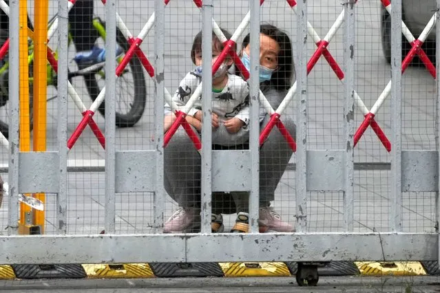A resident and a child look out through gaps in the barriers at a closed residential area during lockdown, amid the coronavirus disease (COVID-19) pandemic, in Shanghai, China, May 10, 2022. (Photo by Aly Song/Reuters)