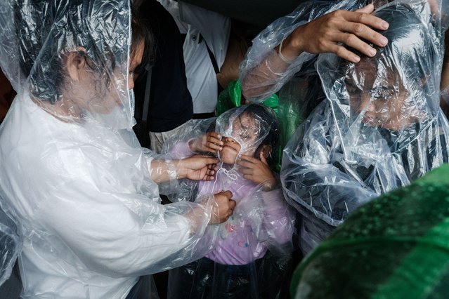 Members of a family take shelter from the rain as they join farmers and their families during a protest against what they described as the government's failure to implement agrarian reforms as they commemorate the Indonesian National Farmers' Day in front of the parliament building in Jakarta on September 24, 2024. (Photo by Yasuyoshi Chiba/AFP Photo)