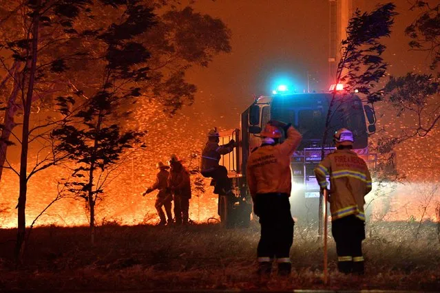 Firefighters hose down trees as they battle against bushfires around the town of Nowra in the Australian state of New South Wales on December 31, 2019. Thousands of holidaymakers and locals were forced to flee to beaches in fire-ravaged southeast Australia on December 31, as blazes ripped through popular tourist areas leaving no escape by land. (Photo by Saeed Khan/AFP Photo)
