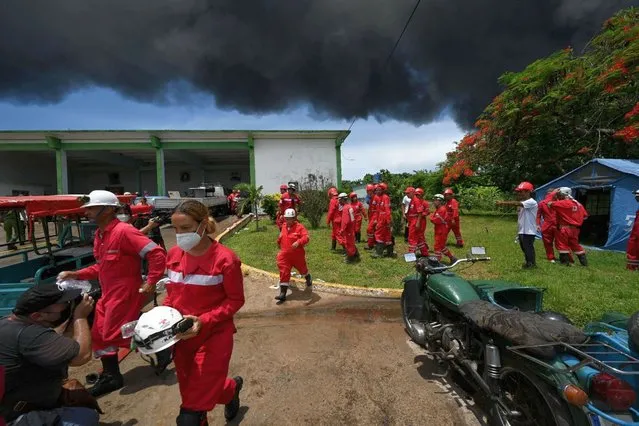 Firefighters are seen near the fire on oil tanks in Matanzas, Cuba, on August 6, 2022. The fire caused by lightning on Friday in a fuel depot in Matanzas, in western Cuba, spread to a second tank at dawn this Saturday and caused 49 injuries, official sources reported. (Photo by Yamil Lage/AFP Photo)