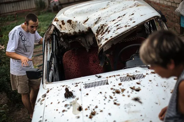 Alexey Danilenko (23) with his neighbor show damaged car after fighting between militants and Ukrainian forces in eastern Ukrainian village Seleznevka, near of Slaviansk, Ukraine, 17 August 2014. Alexey Danilenko and his family were in Seleznevka during fierce fighting between militants and Ukrainian forces. Alexey said, that more than 80 percent buildings in village were damage. (Photo by Roman Pilipey/EPA)