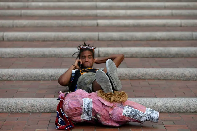 A protester reclines on a set of stairs using a Donald Trump pig puppet as a footrest during a break from protesting at the Republican National Convention in Cleveland, Ohio, U.S., July 21, 2016. (Photo by Andrew Kelly/Reuters)