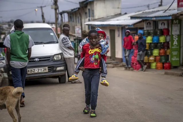 A boy carries a baby on his back on a street in the Kibera area of Nairobi, Kenya Friday, August 12, 2022. (Photo by Ben Curtis/AP Photo)