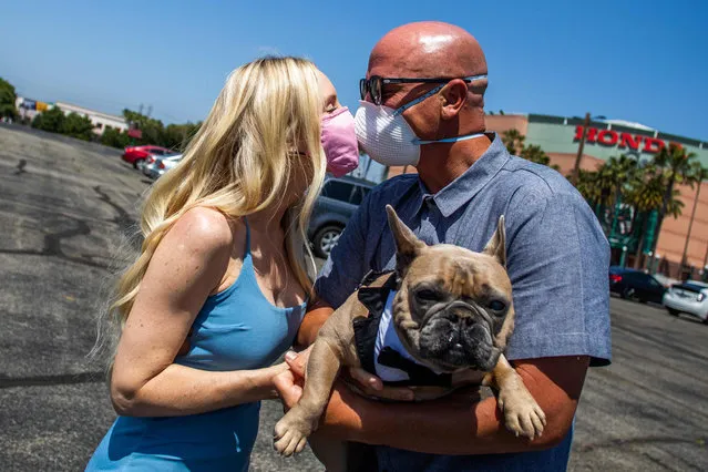 Chad Robbins and Tracey Robbins (R) kiss wearing face masks and holding their dog Huggy after their wedding ceremony officiated by a clerk recorder at the Honda Center parking lot on April 21, 2020 in Anaheim, California. The County of Orange Clerk Recorder employees implemented a variety of social distancing techniques to safely issue licenses and marry couples during the novel coronavirus pandemic. (Photo by Apu Gomes/AFP Photo)