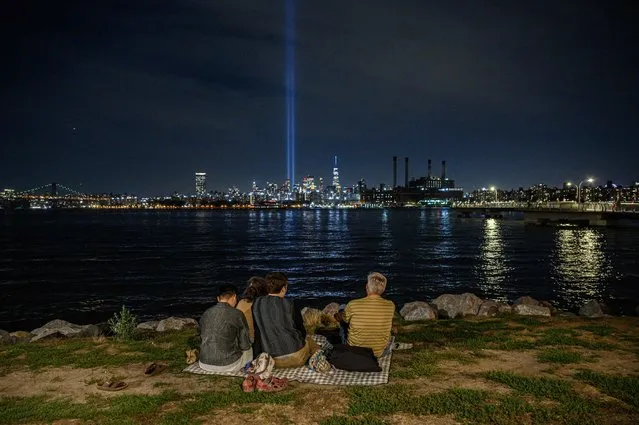 People sit before the east river and the “Tribute in Light” installation amid the Manhattan city skyline commemorating the 9/11 terrorist attacks, in New York on September 10, 2022. (Photo by Ed Jones/AFP Photo)