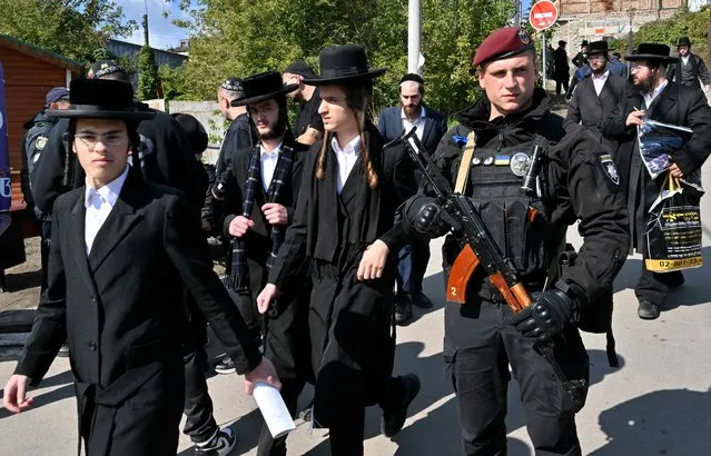 An armed police officer stays in guard as Hasidic Jewish pilgrims walk after pray at tomb of Rabbi Nachman for Rosh Hashana, the Jewish new year, in town of Uman, some 200km from Ukrainian capital of Kyiv on September 25, 2022. Tens of thousands of Jewish pilgrims flock despite war to Ukrainian city of Uman for their annual pilgrimage to Rabbi Nachman from Breslov (1772-1810), founder of an ultra-Orthodox movement that settled in Uman in the early 1800s. (Photo by Sergei Supinsky/AFP Photo)