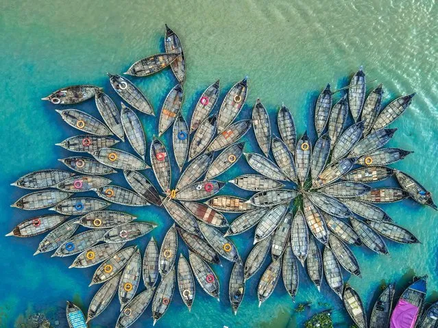 Hundreds of wooden boats resemble like flowers in Dhaka River Port, Bangladesh as they fan out around their moorings on August 18, 2022. The boats, decorated with colourful patterned rugs, are ready to transport workers from the outskirts of the city to their jobs in the centre. The Buriganga river is used as a route into Dhaka city for millions of workers every day. The Bangladeshi capital is one of the most densely populated in the world and home to around 19 million people. (Photo by Mustasinur Rahman Alvi/Rex Features/Shutterstock)