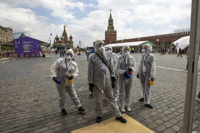 Volunteers wearing face masks, gloves and protective gear to protect against coronavirus, gather to clean an area of an outdoor book market set up at Red Square with GUM, State Department store, left, St. Basil's Cathedral, center, Spasskaya Tower, second with, and the Kremlin Wall, right, in Moscow, Russia, Saturday, June 6, 2020. Muscovites clad in face masks and gloves ventured into Red Square for an outdoor book market, a small sign of the Russian capital's gradual efforts to open up amid coronavirus concerns. (Photo by Alexander Zemlianichenko/AP Photo)