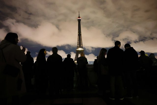People look on the Eiffel Tower with lights switched off to mark Earth Hour 2025 in Paris, France, 22 March 2025. Earth Hour is held annually as a symbol of commitment to the planet by encouraging individuals, communities and businesses to give one hour to the Earth by switching off non-essential electric lights. (Photo by Mohammed Badra/EPA/EFE)
