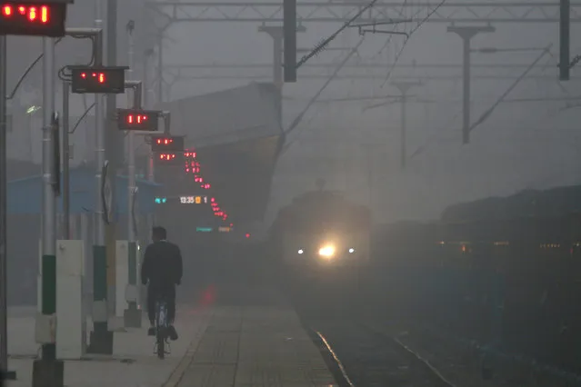 A man paddles his bicycle on a platform as a train moves through fog on a cold morning at a railway station in Chandigarh, India, December 13, 2017. (Photo by Ajay Verma/Reuters)