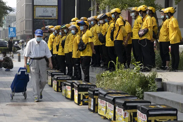 An elderly man wearing a mask to curb the spread of the coronavirus pulls along a shopping cart past delivery men gathered for a briefing before work in Beijing Thursday, July 23, 2020. (Photo by Ng Han Guan/AP Photo)
