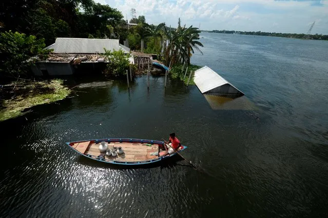 A man paddles a boat next to a submerged home in a flooded area due to recent monsoon rainfalls in Dhamrai on August 11, 2020. (Photo by Munir Uz Zaman/AFP Photo)