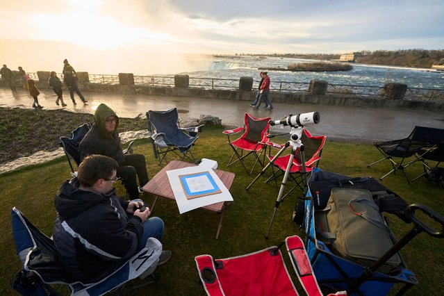 People sit next to the Horseshoe Falls in Niagara Falls, Ontario, Canada, on April 8, 2024 as they prepare for the total eclipse which is set to pass over the region later in the day. This year's path of totality is 115 miles (185 kilometers) wide and home to nearly 32 million Americans, with an additional 150 million living less than 200 miles from the strip. The next total solar eclipse that can be seen from a large part of North America won't come around until 2044. (Photo by Geoff Robins/AFP Photo)